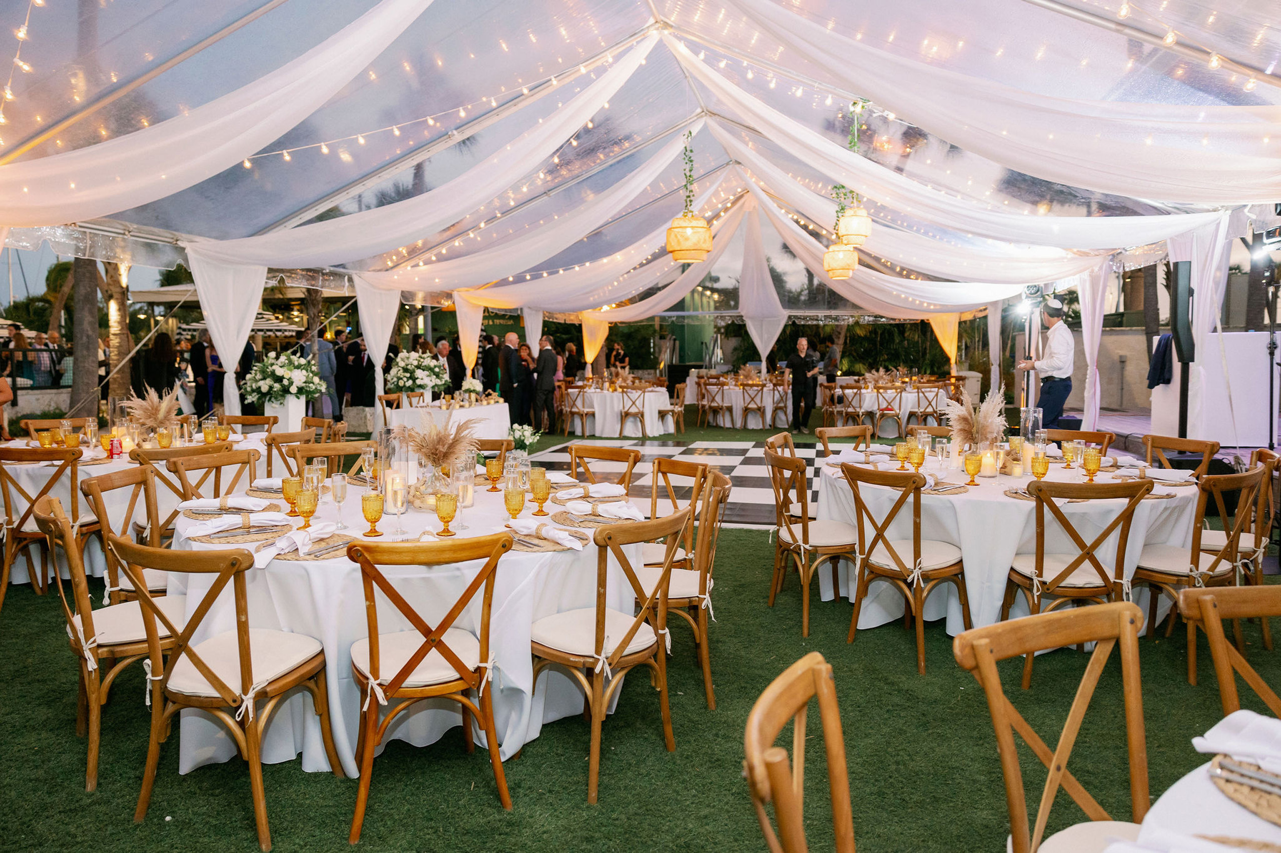 Elegant outdoor lawn wedding under draped tent with lights.