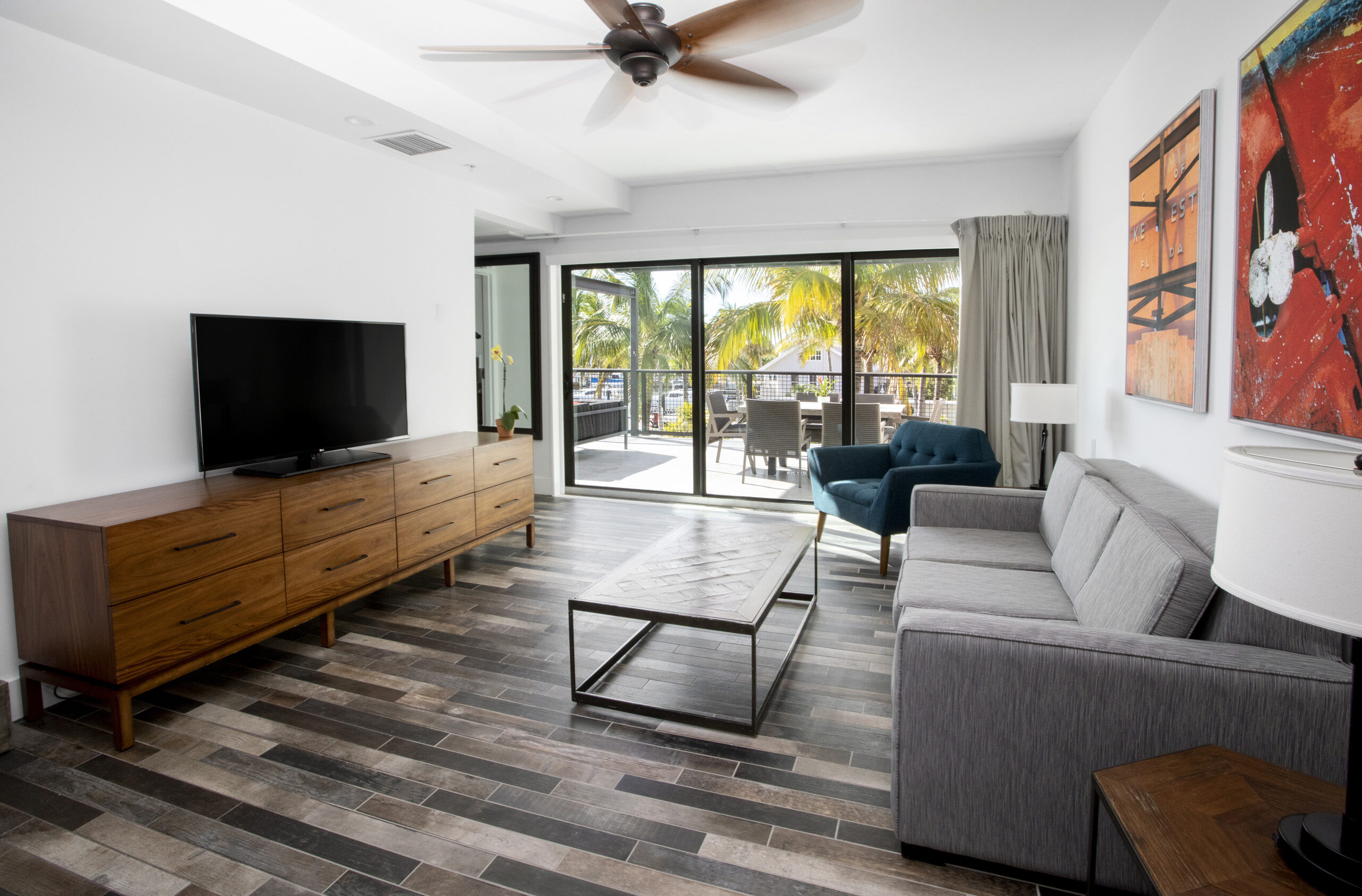 Living area with gray sofa, blue armchair, TV on wooden dresser, and sliding doors to balcony.