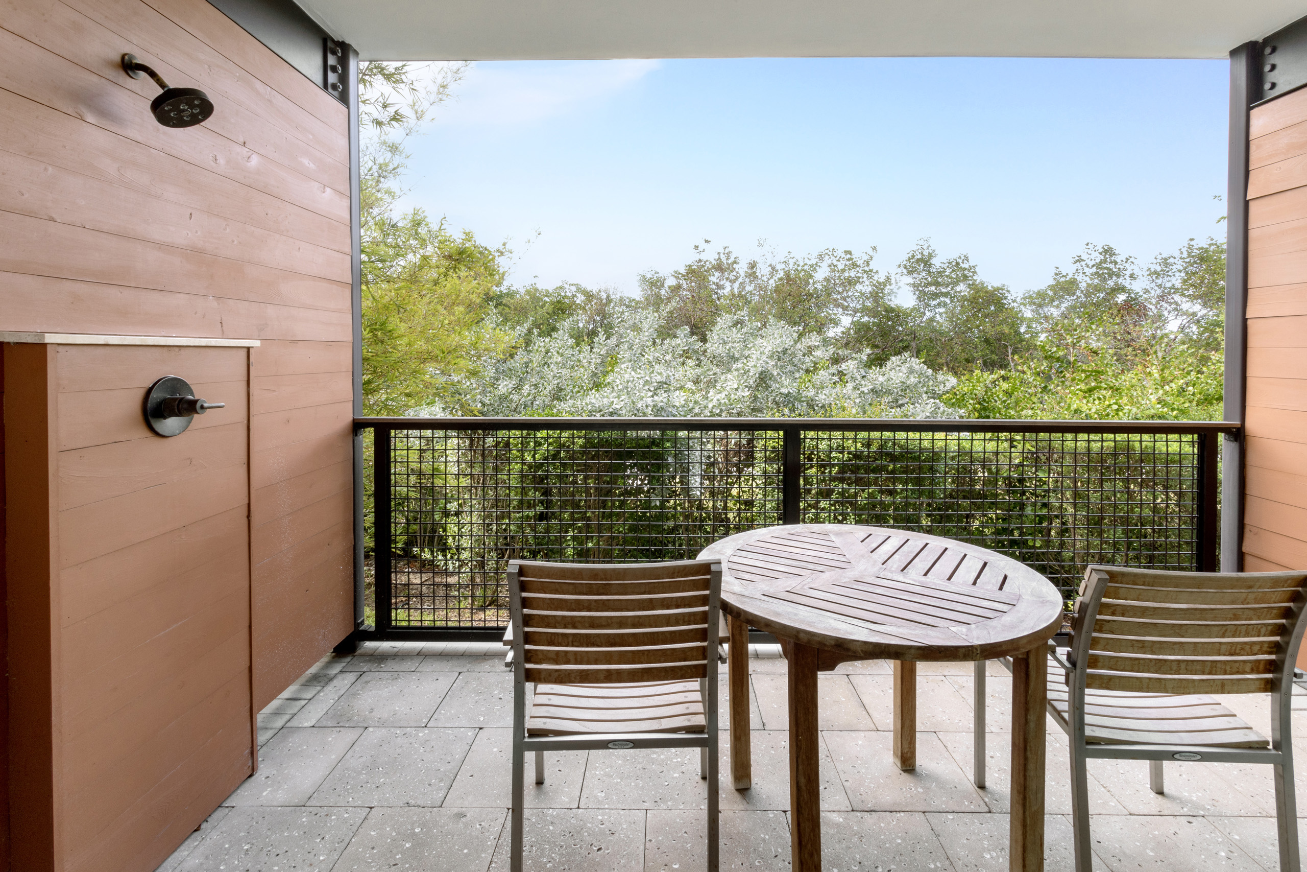 Balcony with wooden table, chairs, overlooking lush mangroves.