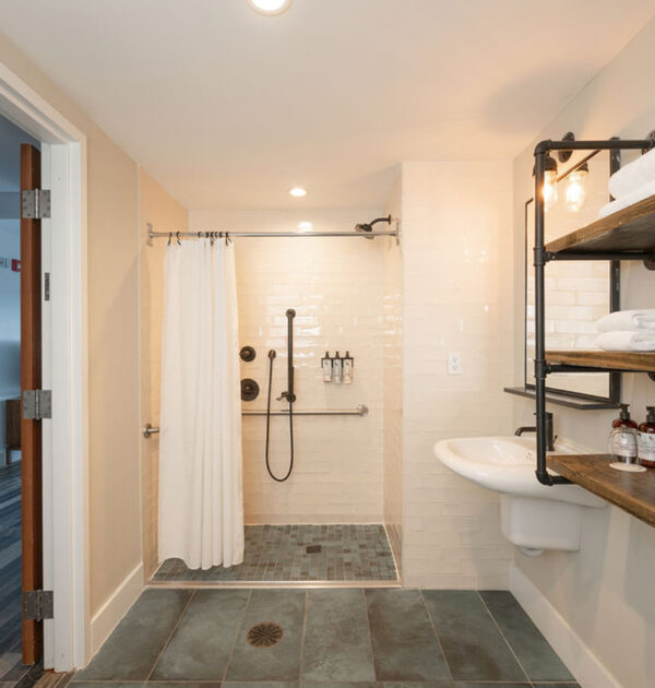 Accessible hotel bathroom with roll-in shower and shelving.