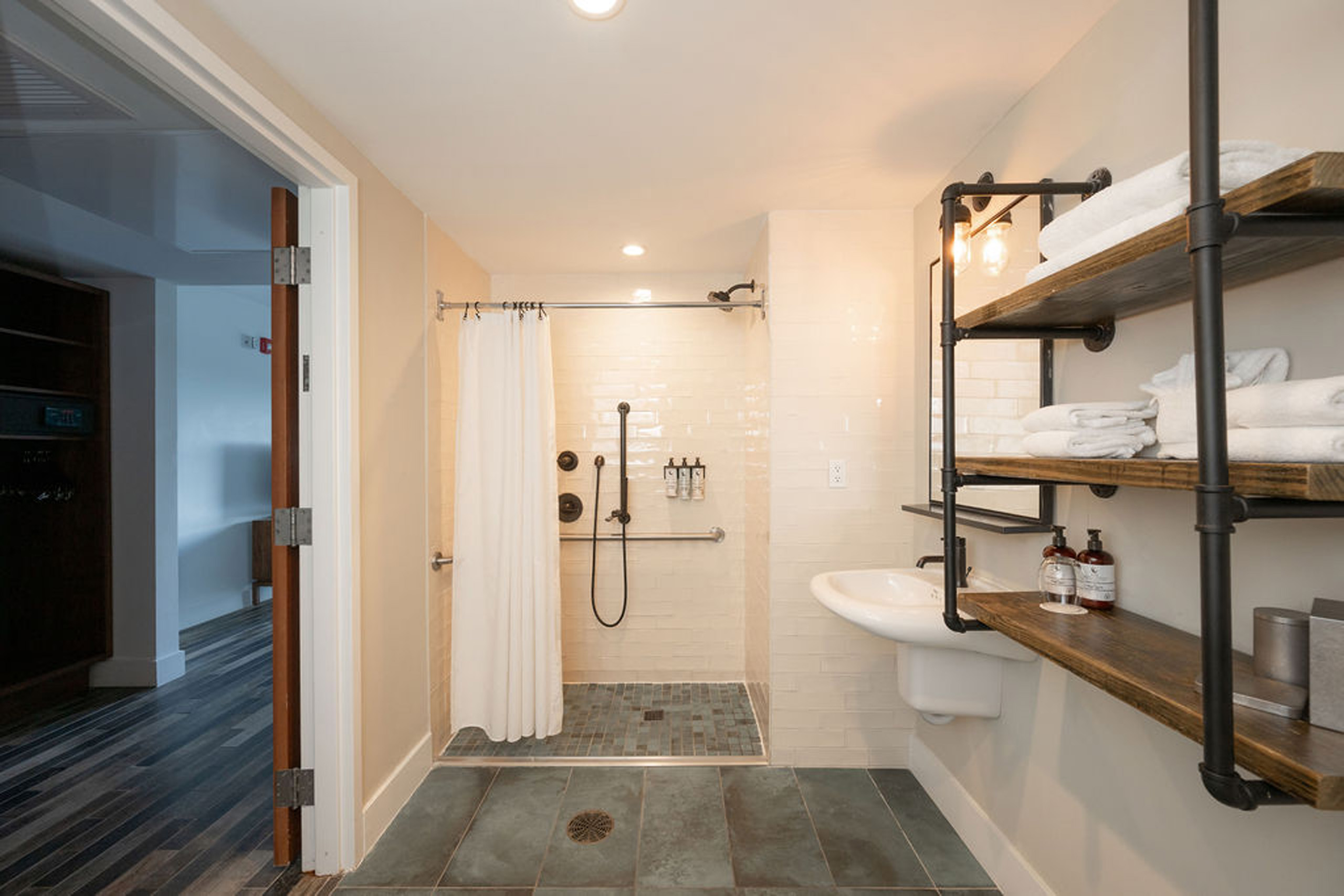 Accessible hotel bathroom with roll-in shower and shelving.