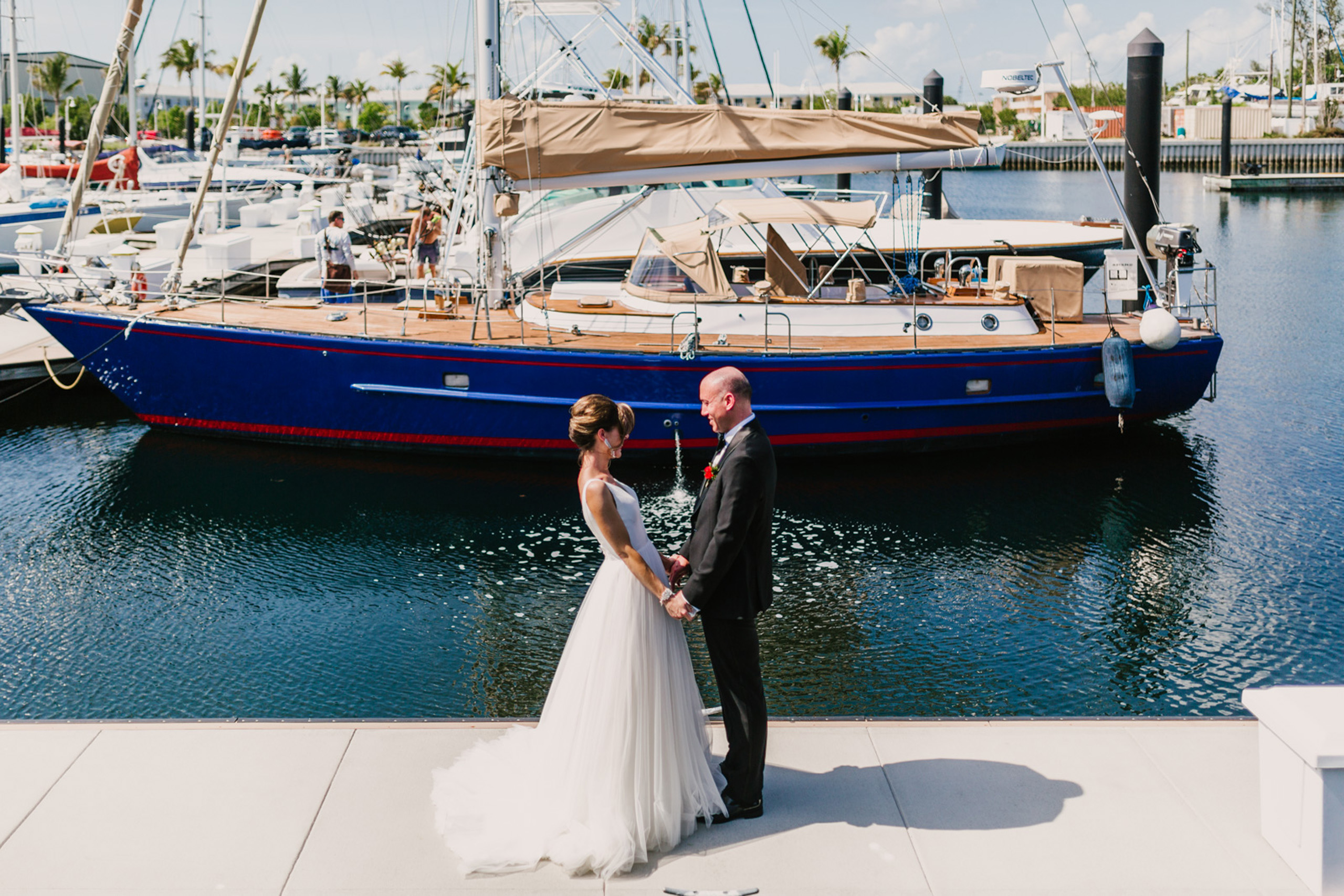 Bride and groom holding hands beside sailboat.