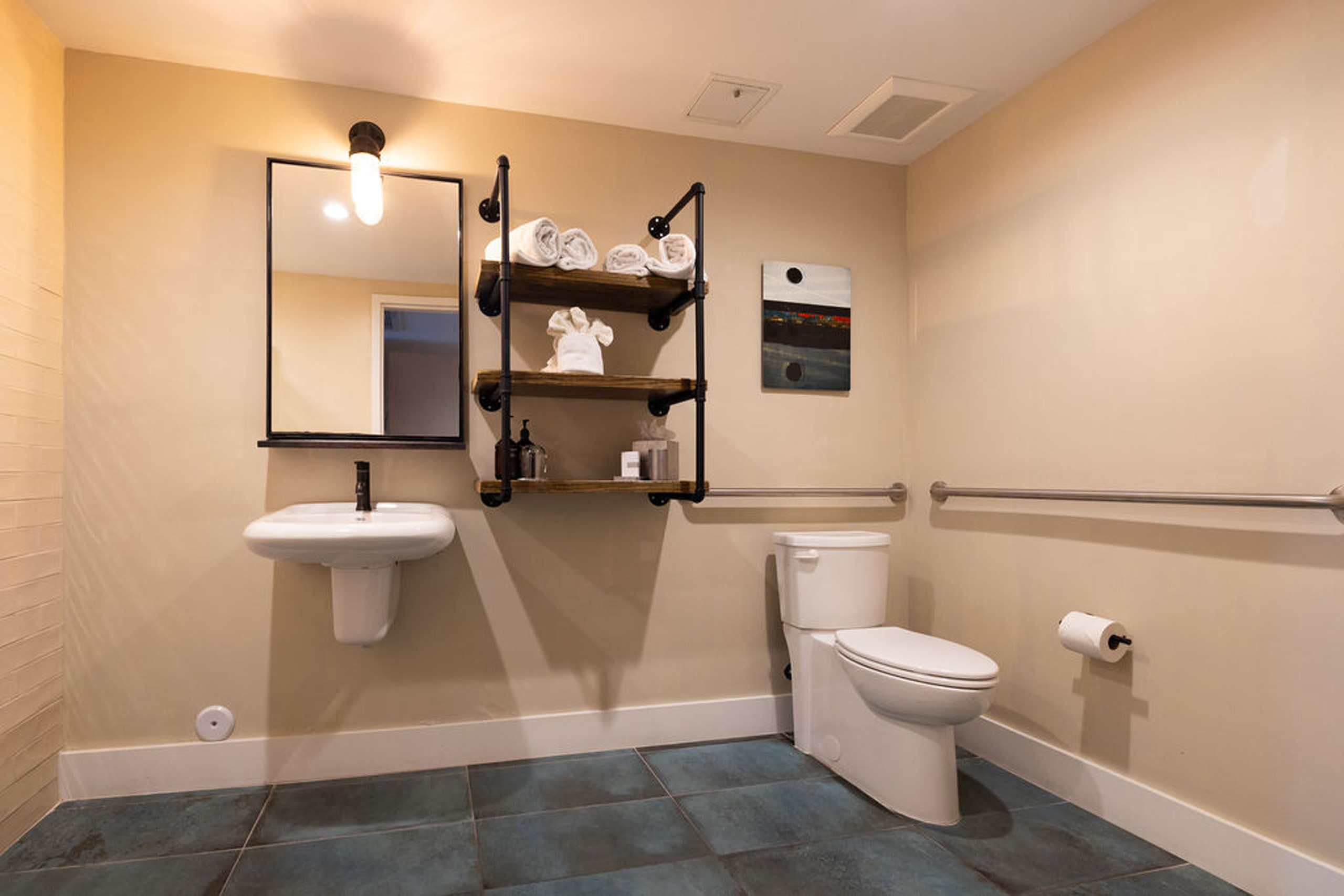 Accessible bathroom with mounted sink, toilet, towel rack, and shelving.