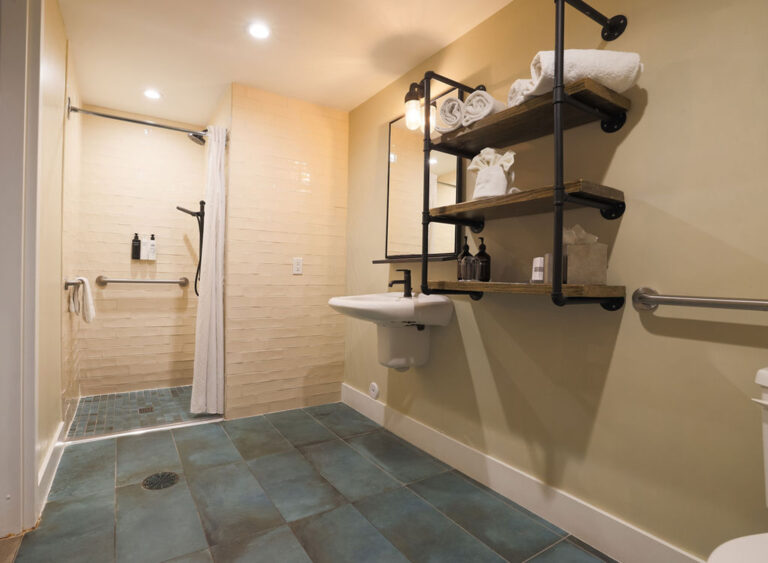 Roll-in shower with grab bars, handheld showerhead, and tiled floor.