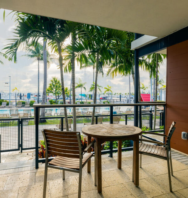 Private balcony with table and two chairs, pool and palm views.