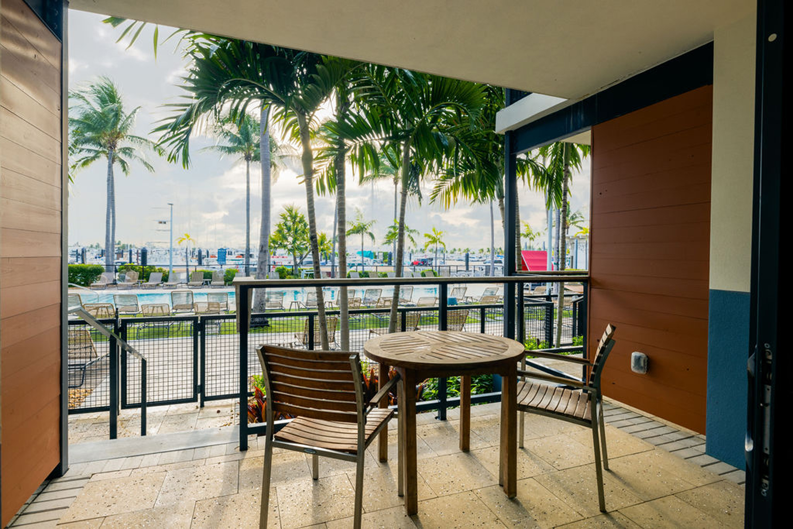 Private balcony with table and two chairs, pool and palm views.