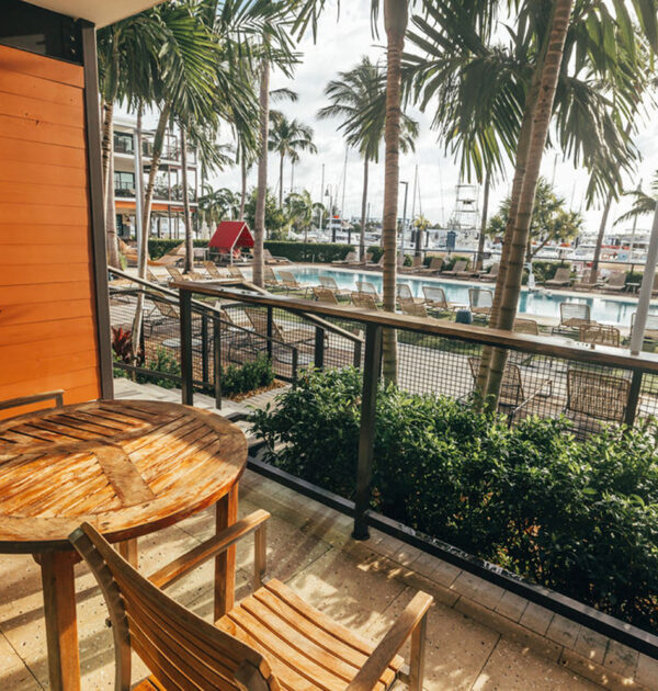 Patio with table and chairs, overlooking pool loungers, palm trees, and marina.
