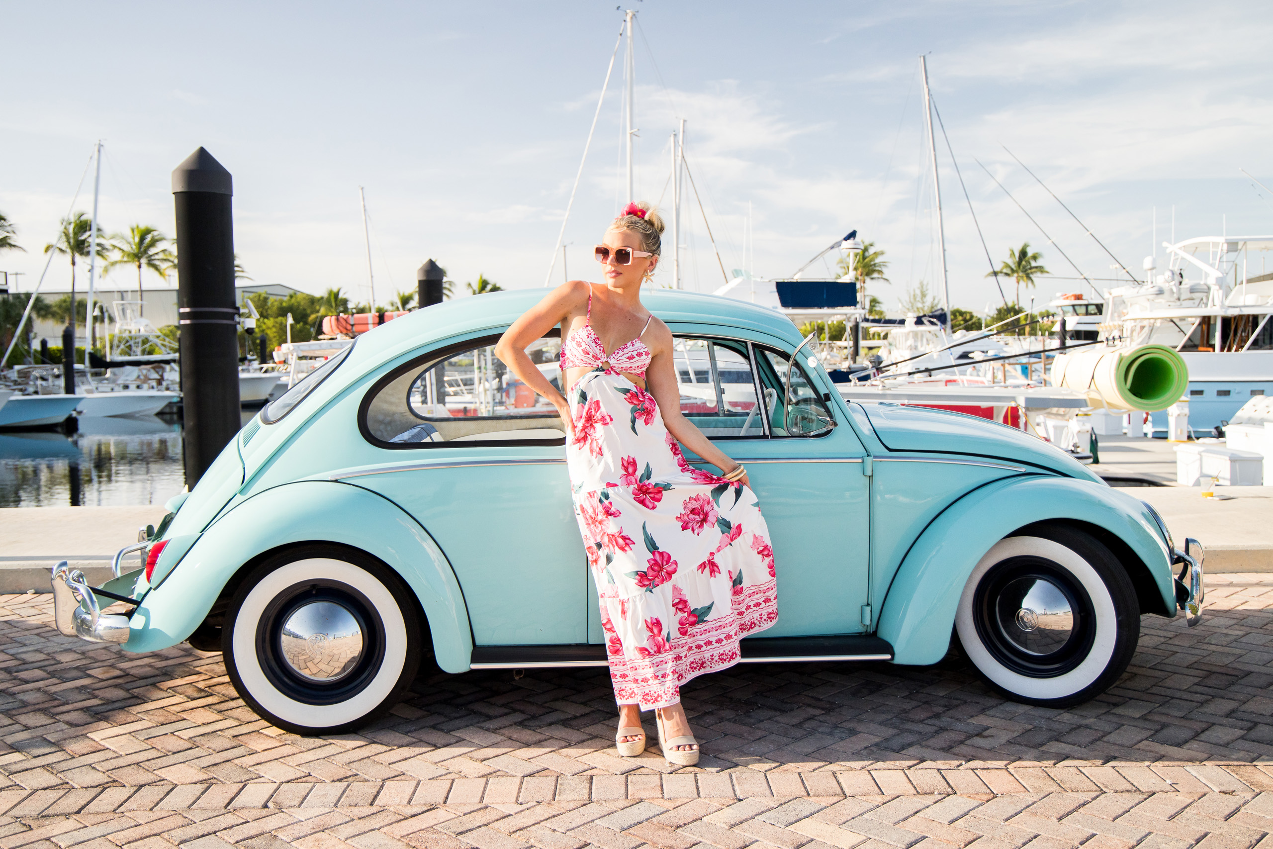 Woman in floral dress poses by vintage turquoise car.