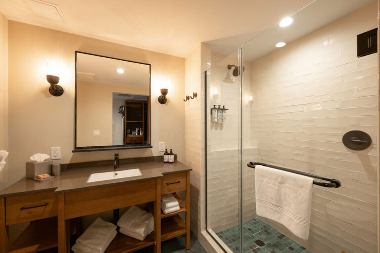 Bathroom with vanity, mirror, sconces, and glass shower enclosure.