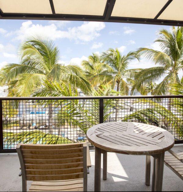 Balcony with wooden table, two chairs, and palm tree views.