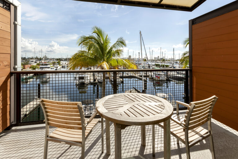 Balcony with wooden table, two chairs, overlooking marina and boats.