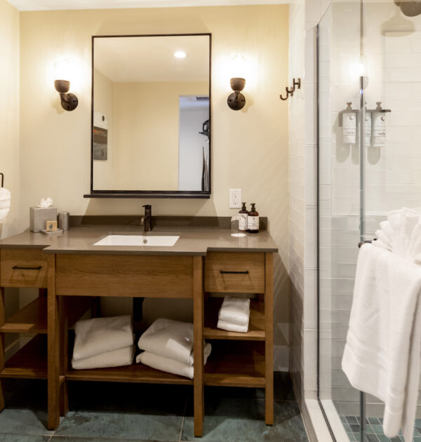 Bathroom with wooden vanity, mirror, towels, and tiled shower.