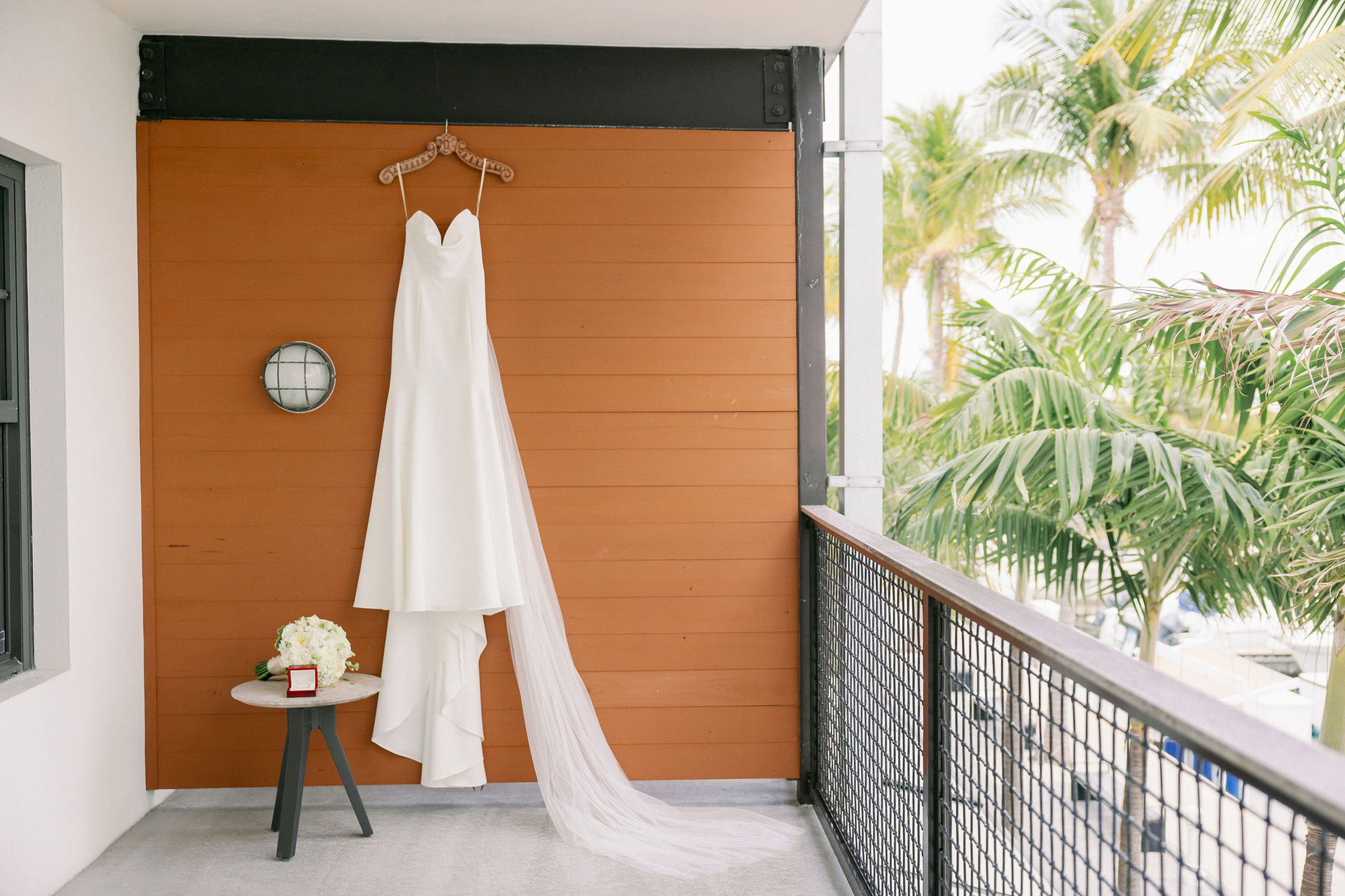 White wedding dress with long veil hanging on balcony wall.