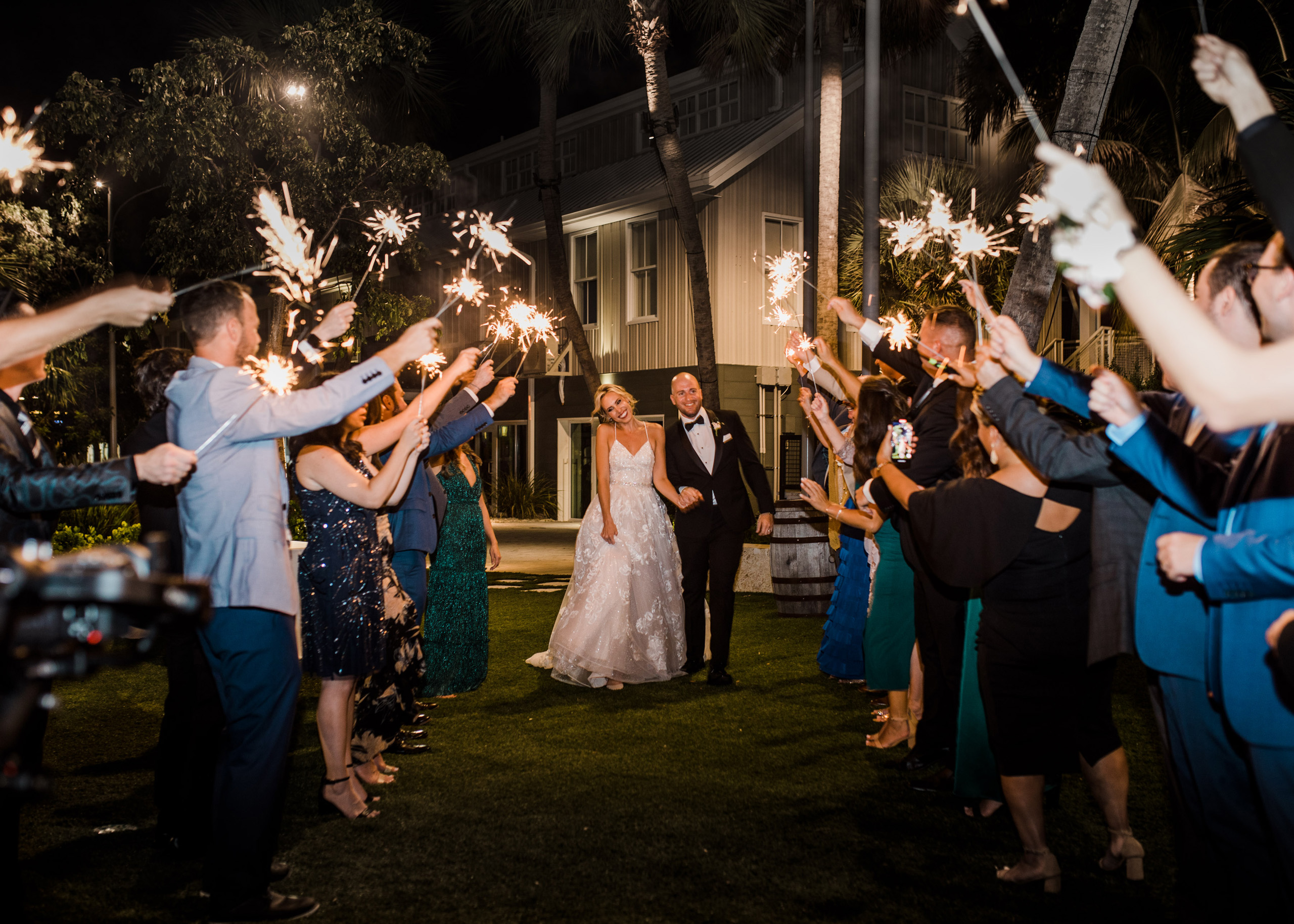 Couple’s sparkler exit at night with guests cheering.