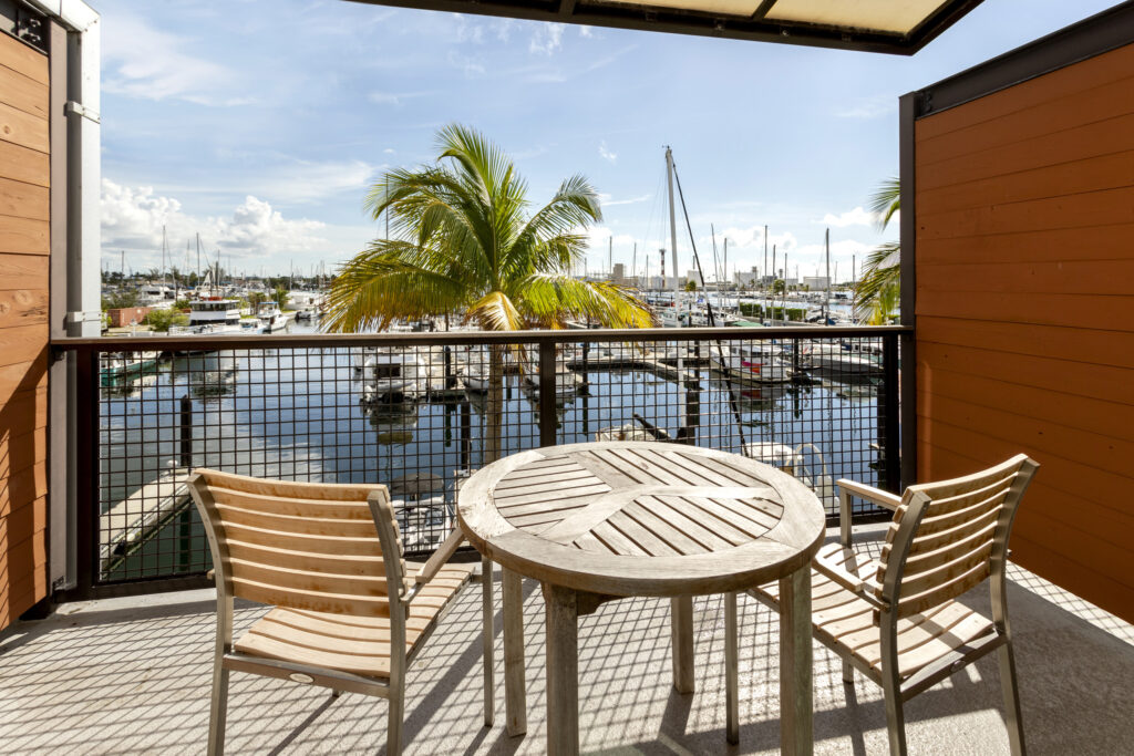 Wooden chairs on balcony overlooking marina with sailboats.