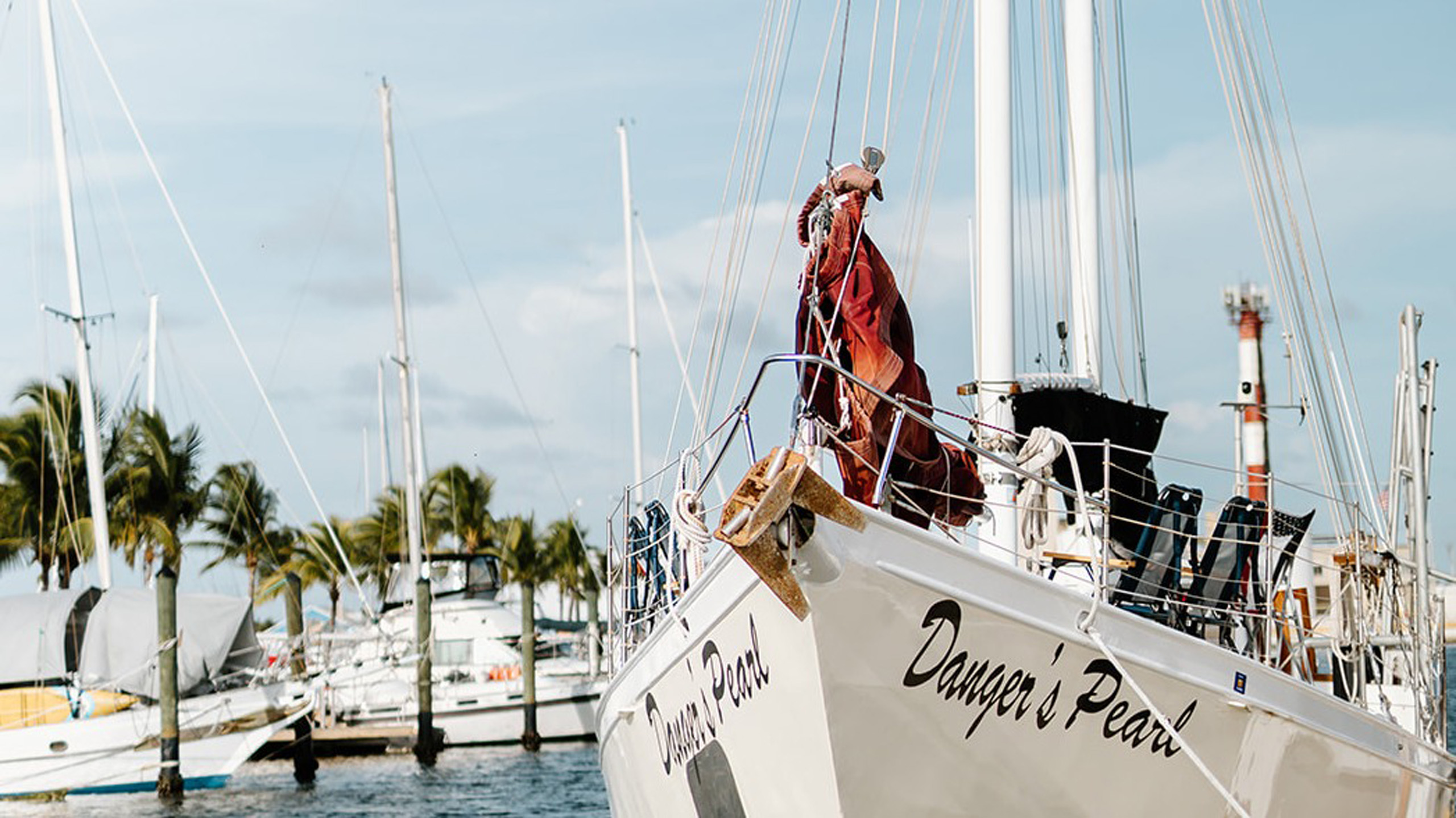 Sailboat named Danger’s Pearl docked at marina with sails tied.
