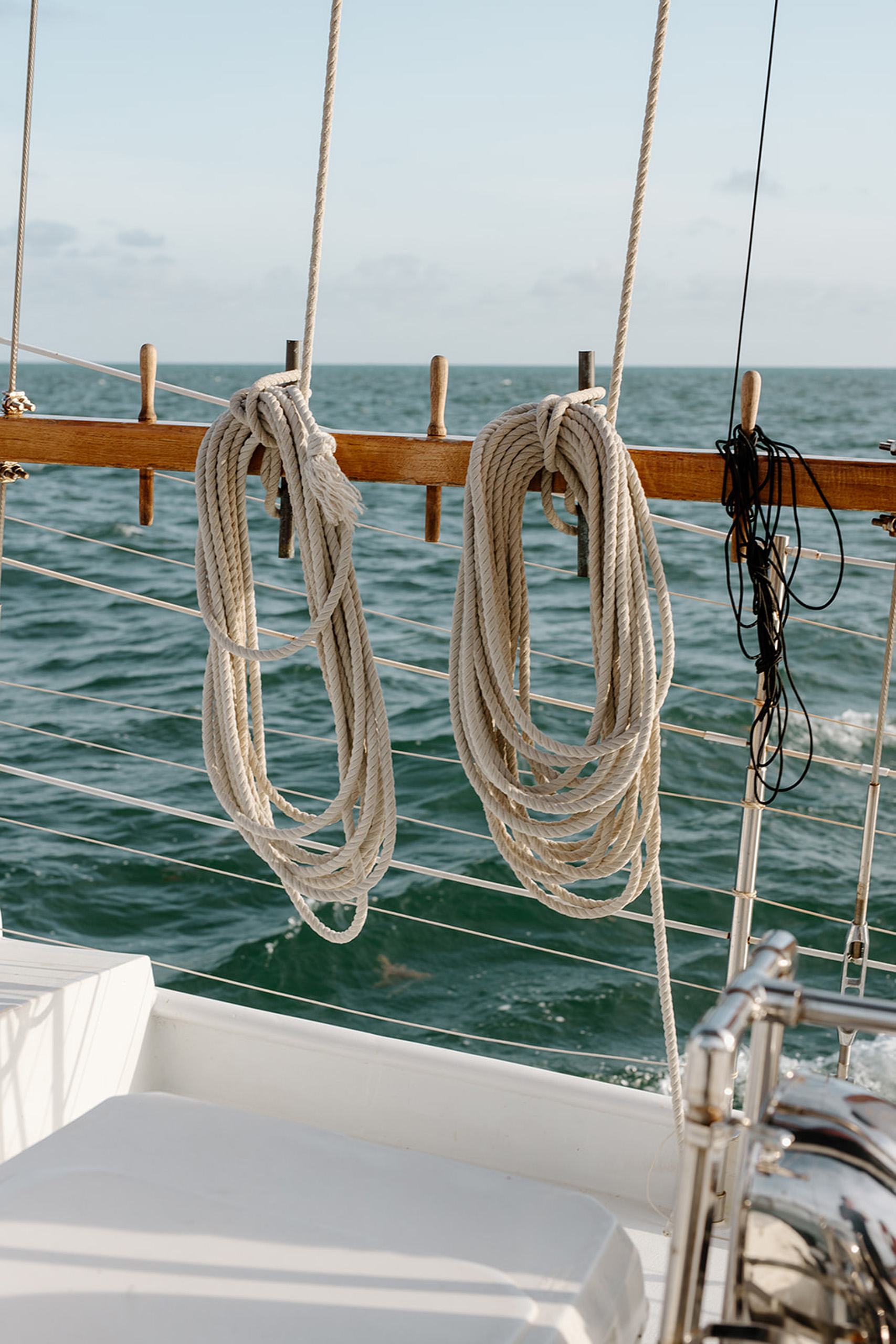 Coiled sailing ropes hanging on boat railing at sea.