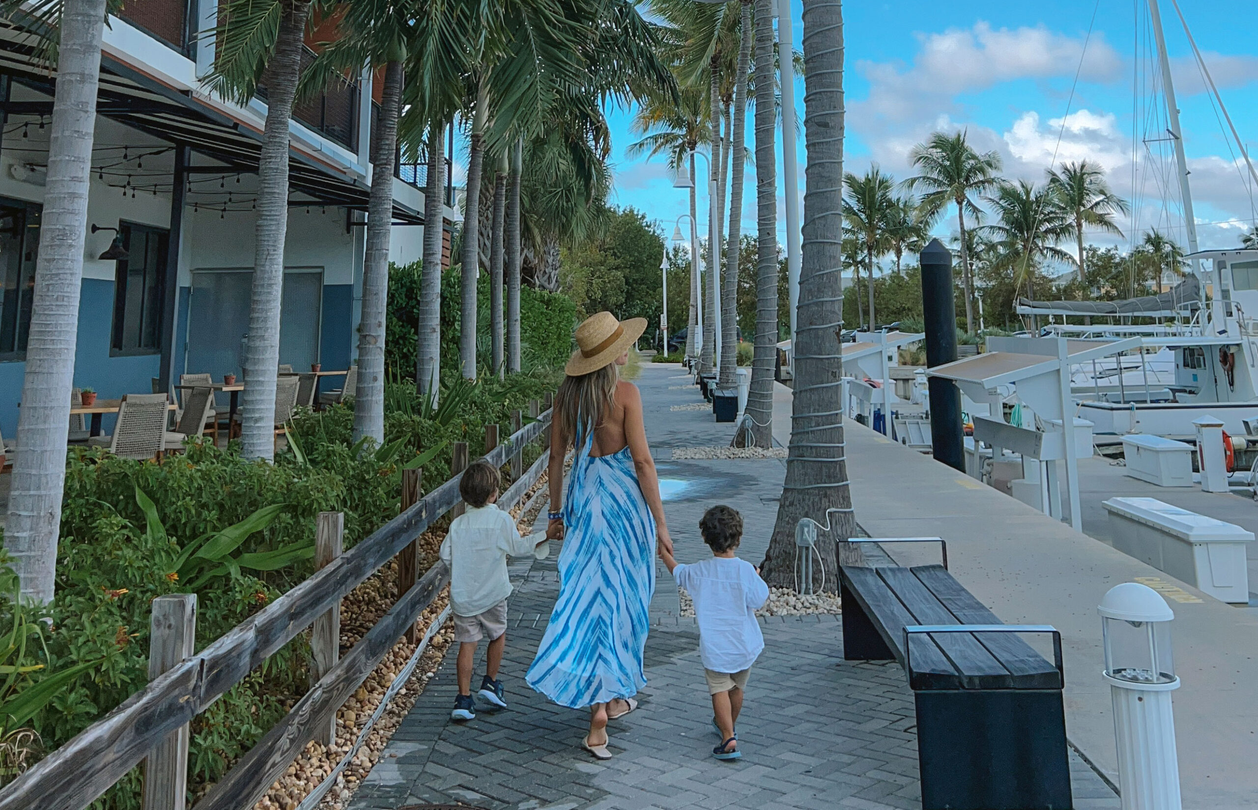 Woman with two children walking along palm-lined marina path.